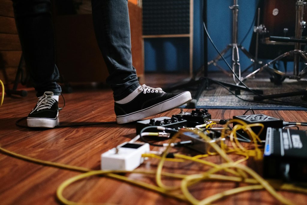 Close-up of a musician's feet surrounded by pedals and wires in a music studio.